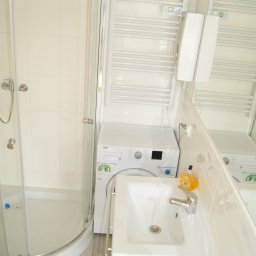 BUKU KRZYSZTOF KOCZYŁO - Jasna łazienka z kabiną prysznicową, pralką pod umywalką i grzejnikiem drabinkowym. Widoczna butelka z mydłem w płynie o zapachu pomarańczy.