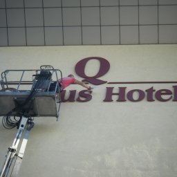 BUKU KRZYSZTOF KOCZYŁO - Pracownik na podnośniku koszowym montuje literę 'Q' na elewacji budynku 'Qus Hotel'.