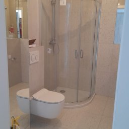 MARCIN GRULKOWSKI - Nowoczesna łazienka po remoncie: kabina prysznicowa, podwieszana toaleta, beżowe płytki z drobnym wzorem. Widoczne odbicie w lustrze.