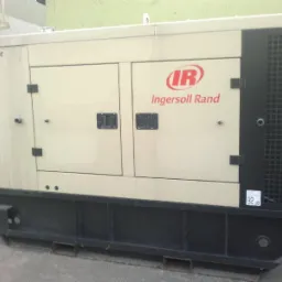 Stacjonarny generator prądu Ingersoll Rand G60 w beżowo-czarnej obudowie, widoczny z boku, na zewnątrz budynku.
