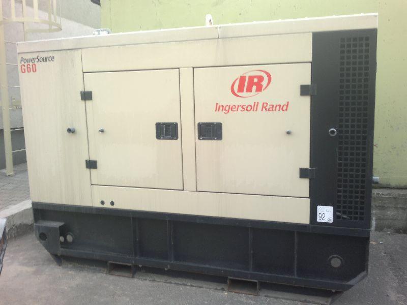 Stacjonarny generator prądu Ingersoll Rand G60 w beżowo-czarnej obudowie, widoczny z boku, na zewnątrz budynku.