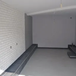 Wnętrze pomieszczenia po pracach wykończeniowych w Gaworzycach: biała ściana z imitacją cegły, szara podłoga z ciemnymi listwami, surowe szare ściany, widoczny fragment instalacji elektrycznej.