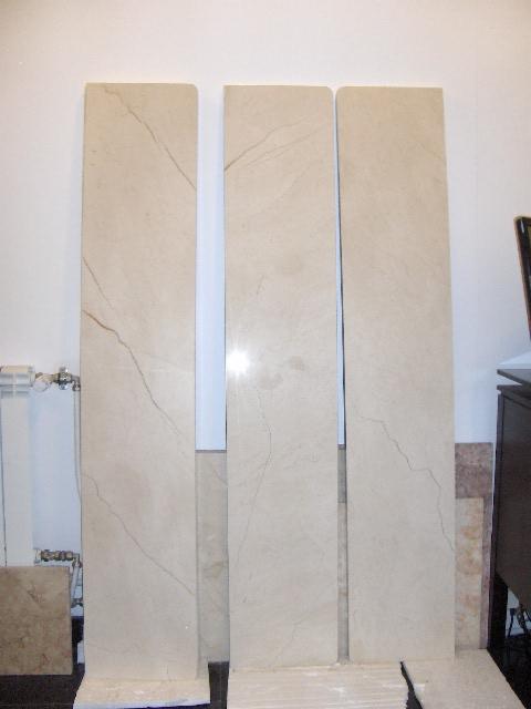 Trzy pionowe płyty parapetów z beżowego kamienia z delikatnym marmurkowym wzorem, ustawione obok siebie na podłodze w pomieszczeniu, prawdopodobnie podczas przygotowania do montażu.
