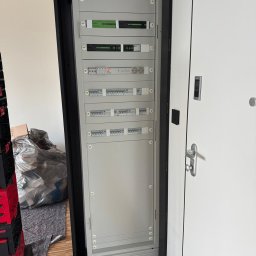 LEDBEST Sp. z o.o. - Rozdzielnica elektryczna w szafie, widoczne zabezpieczenia, moduły sterujące i gniazda. Obok białe drzwi z klamką i panelem sterowania.