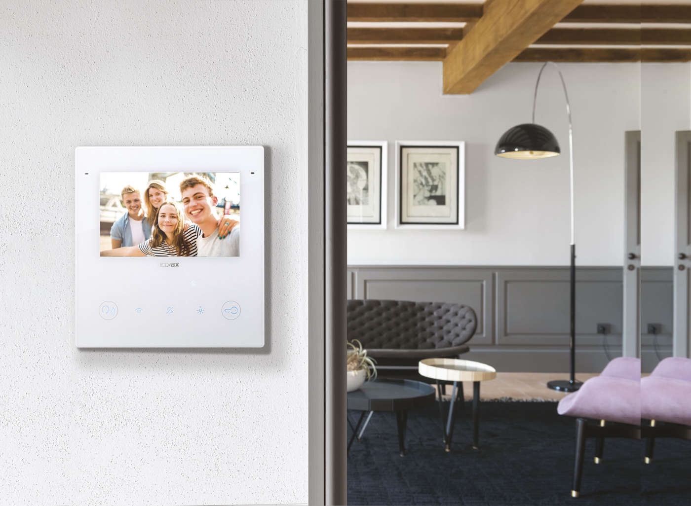 Biały panel wideodomofonu z ekranem LCD prezentującym zdjęcie grupy młodych ludzi, zamontowany na teksturowanej ścianie w nowoczesnym wnętrzu z widocznym salonem w tle.