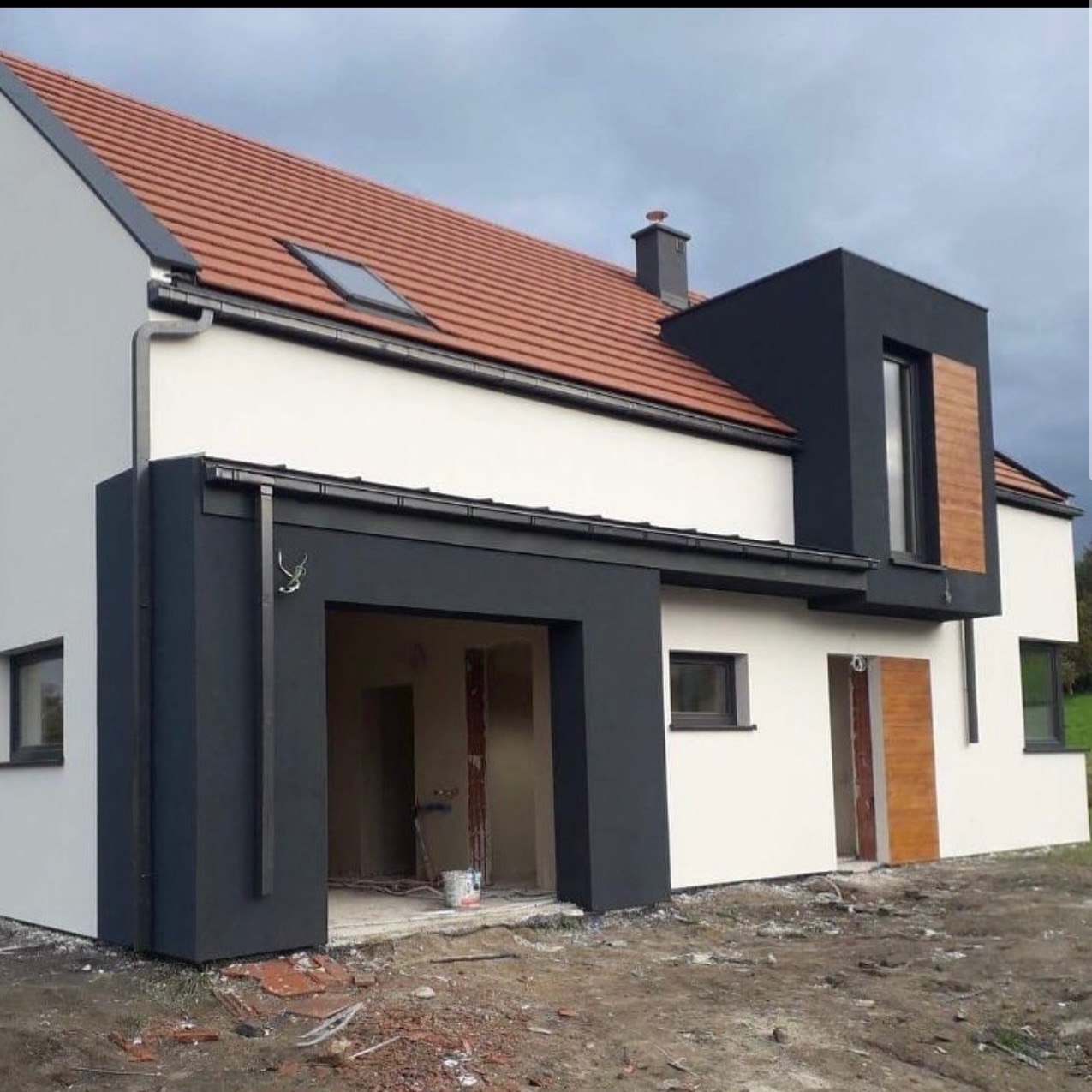 Nowoczesny dom jednorodzinny z białą elewacją i antracytowymi elementami, widok z zewnątrz, teren wokół domu w trakcie prac wykończeniowych.