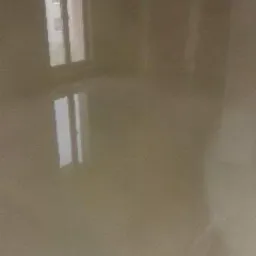 Świeżo wylana, samopoziomująca wylewka podłogowa w jasnym pomieszczeniu z oknem; widoczne odbicie okna w gładkiej powierzchni wylewki.