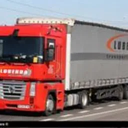 Czerwona ciężarówka z naczepą marki Renault Magnum z logo firmy transportowej LuberdA na boku, jadąca po drodze w słoneczny dzień. Widoczne słupy wysokiego napięcia w tle.