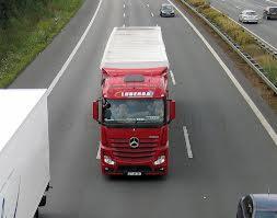 Czerwona ciężarówka Mercedes-Benz z białą naczepą, widziana z góry na autostradzie podczas transportu międzynarodowego.