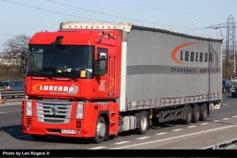 Czerwona ciężarówka z naczepą marki Renault Magnum z logo firmy transportowej LuberdA na boku, jadąca po drodze w słoneczny dzień. Widoczne słupy wysokiego napięcia w tle.