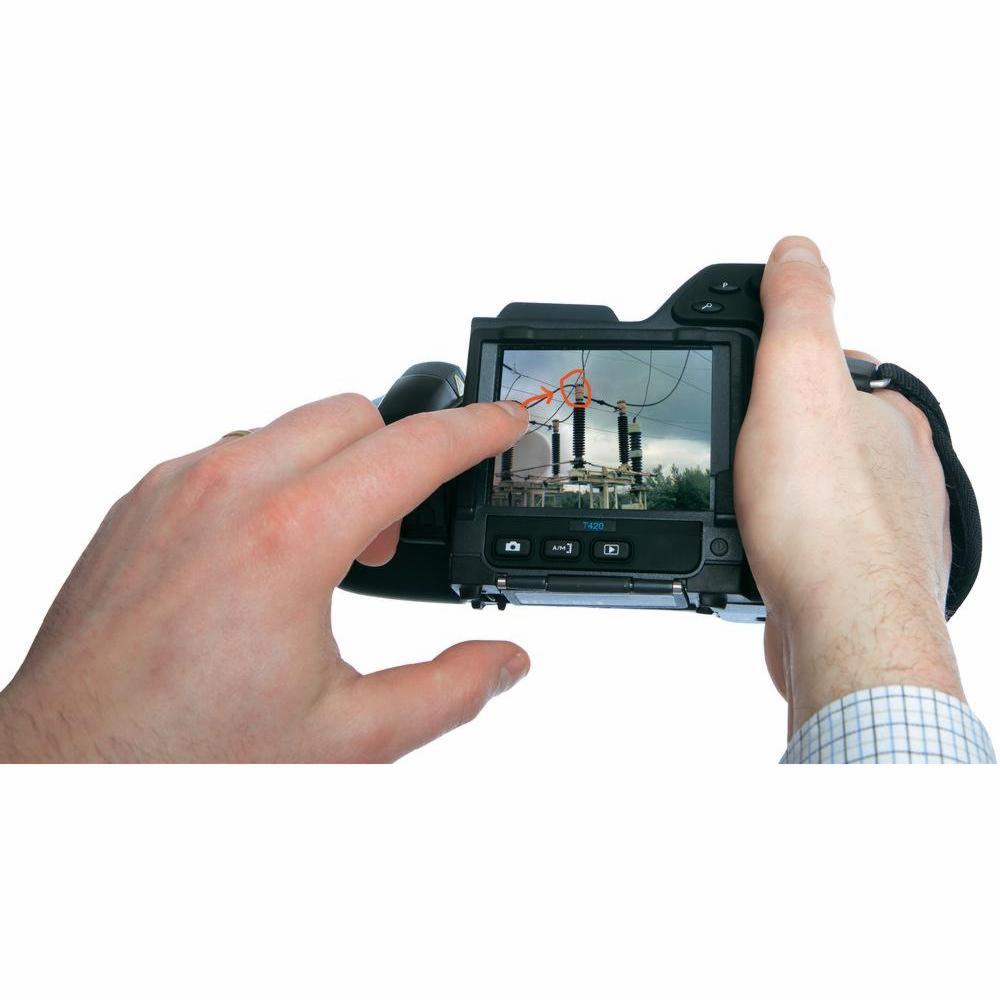 Ręka dotyka ekranu kamery termowizyjnej FLIR T420, na którym widoczny jest obraz transformatora z zaznaczonym punktem pomiaru temperatury.