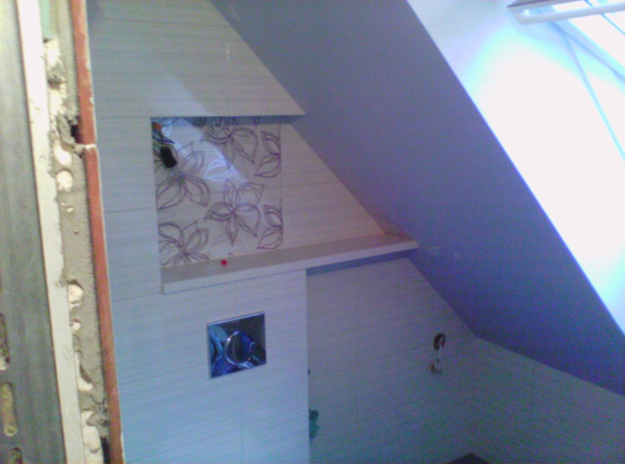 Łazienka na poddaszu w trakcie wykańczania, widoczne płytki z motywem kwiatowym we wnęce, zabudowa WC i fragment ściany z niedokończonymi pracami wykończeniowymi.