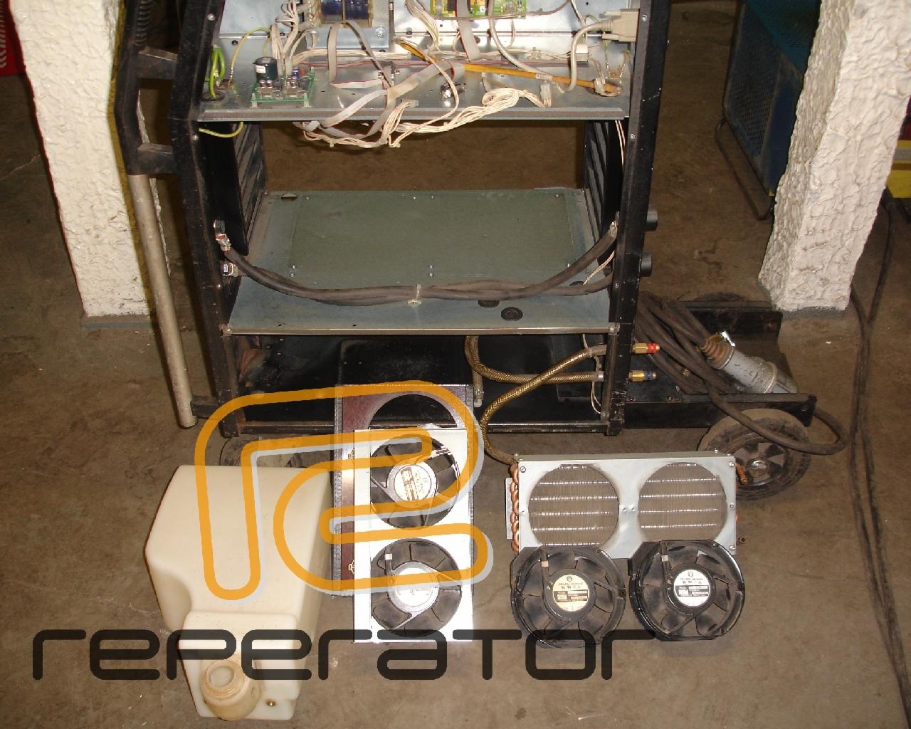 Rozłożona spawarka z widocznymi elementami chłodzenia: wentylatory i zbiornik na płyn chłodzący. Widoczne przewody i elektronika urządzenia.