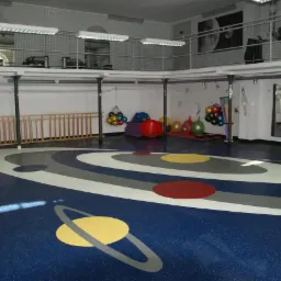 Niebieska posadzka w sali gimnastycznej z motywem Układu Słonecznego, widoczne piłki do ćwiczeń, drabinki i lustro na ścianie.