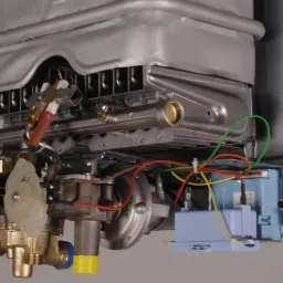 Wnętrze piecyka gazowego Euroterm 275 SEI z widocznymi elementami instalacji, w tym przewodami, zaworami i elektroniką, na szarym tle.