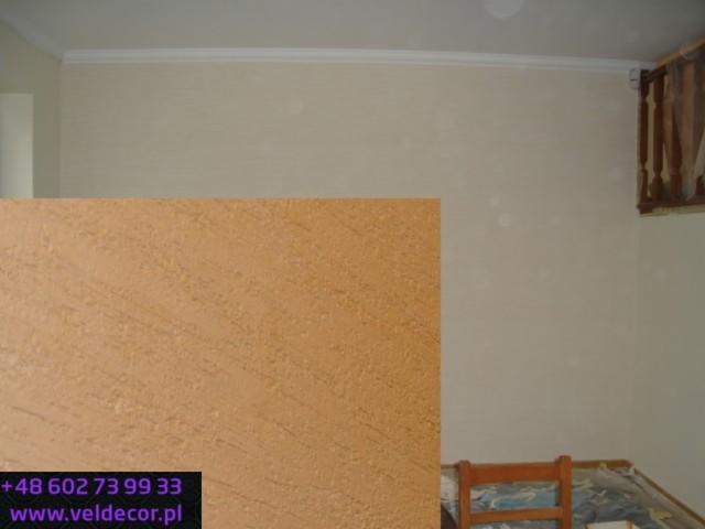 Ściana z dekoracyjną strukturą trawertynu w odcieniach beżu i brązu, widoczna listwa sufitowa i fragment drewnianej balustrady.