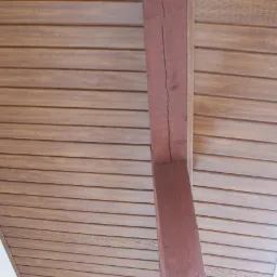 Drewniana podbitka dachowa zamontowana pod okapem, widoczna z perspektywy od dołu, z brązową belką konstrukcyjną i fragmentem rynny