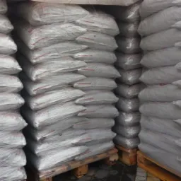 Stosy worków z opałem, owinięte folią, ułożone na paletach. Widoczne czerwone paski na workach.