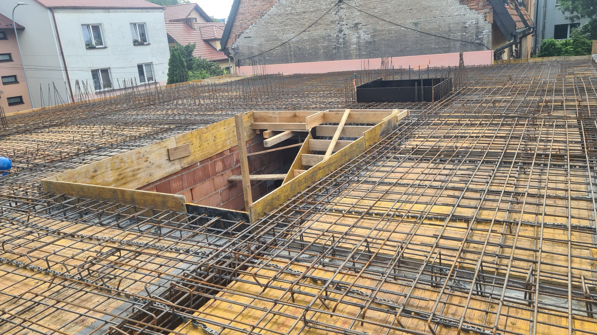 Zbrojenie stropu z deskowaniem i otworem na schody w trakcie budowy domu, widoczne cegły i elementy konstrukcyjne.