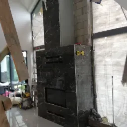 Montaż obudowy kominka z czarnego marmuru z widocznymi przyssawkami na g&oacute;rnej części, w trakcie prac wykończeniowych wnętrza, z widoczną drabiną i narzędziami w tle.