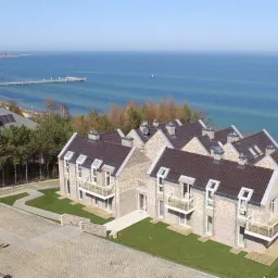 Kompleks apartamentowy z jasnej cegły z balkonami, widok z lotu ptaka na tle morza i molo.