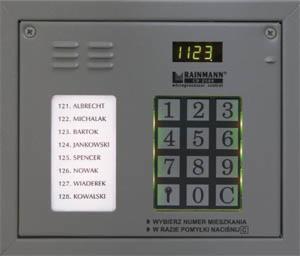 Szary panel domofonu z podświetlaną klawiaturą numeryczną, wyświetlaczem LCD wskazującym numer mieszkania 1123 oraz listą nazwisk lokatorów po lewej stronie.
