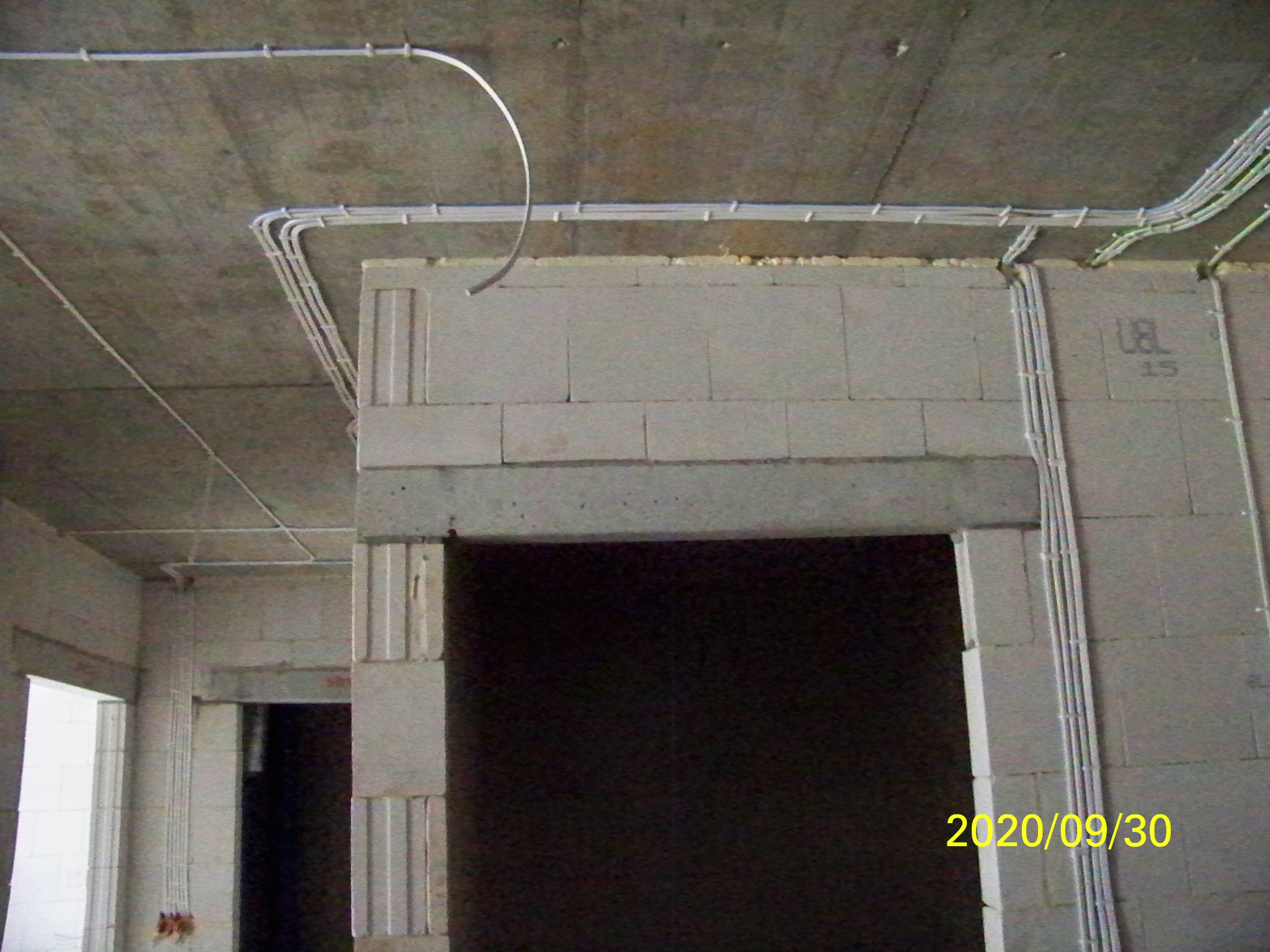 Surowe wnętrze w trakcie budowy z widocznymi przewodami elektrycznymi poprowadzonymi po suficie i ścianach z betonu komórkowego, data na ścianie 2020/09/30.