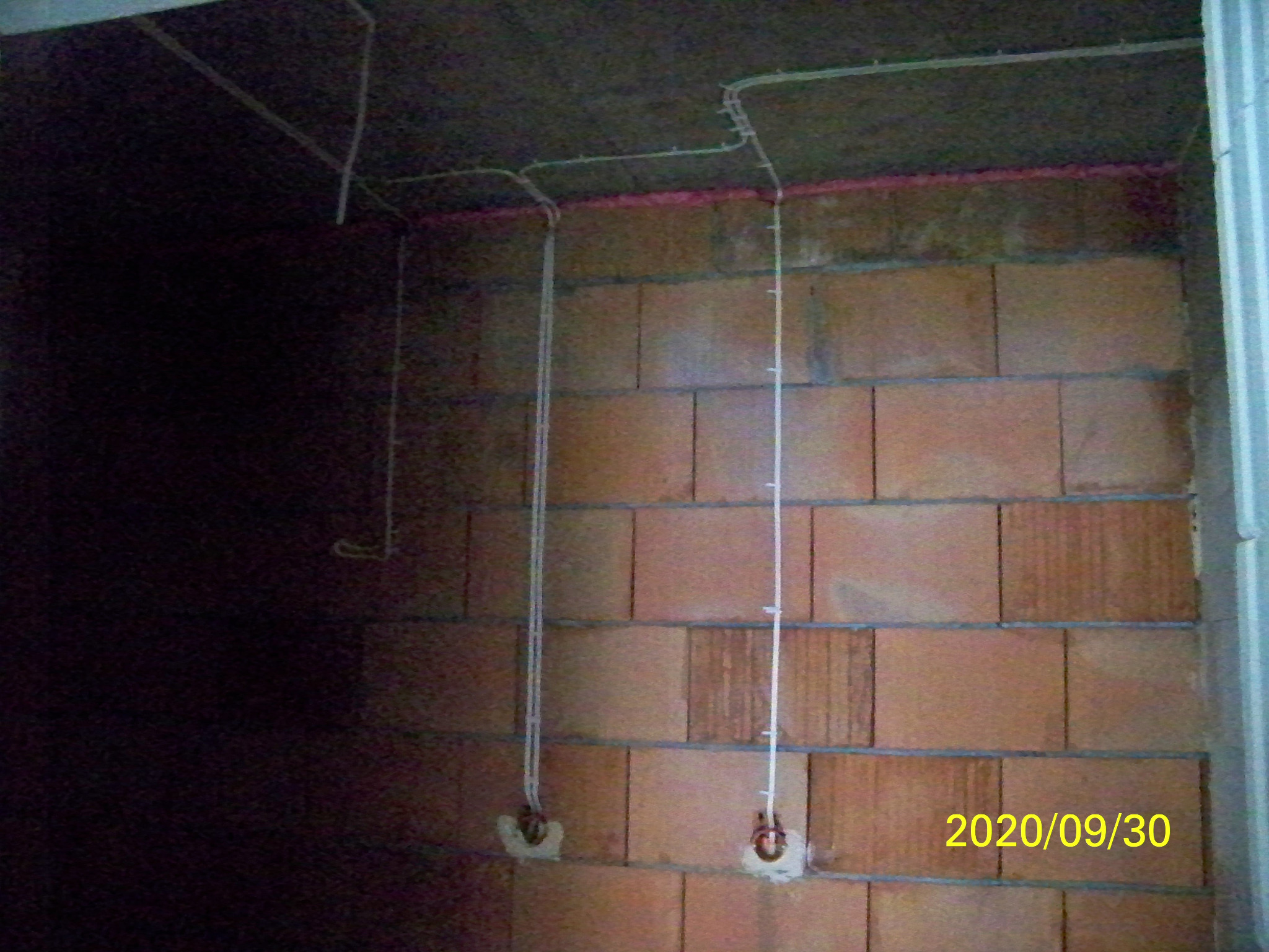 Instalacja elektryczna w surowym wnętrzu: przewody prowadzone po ścianie z cegieł, widoczne puszki pod gniazdka, instalacja pod sufitem, data wykonania zdjęcia widoczna w prawym dolnym rogu.