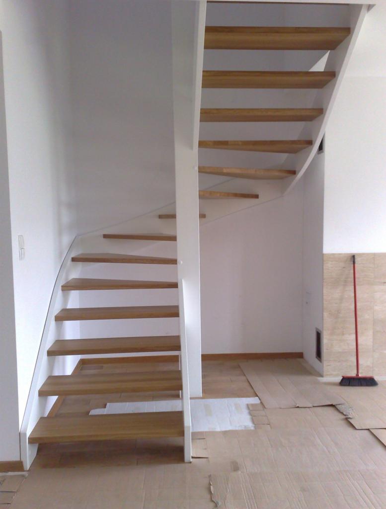 Schody drewniane o konstrukcji wspornikowej, z białymi elementami wykończeniowymi, w trakcie montażu, podłoga zabezpieczona kartonem.