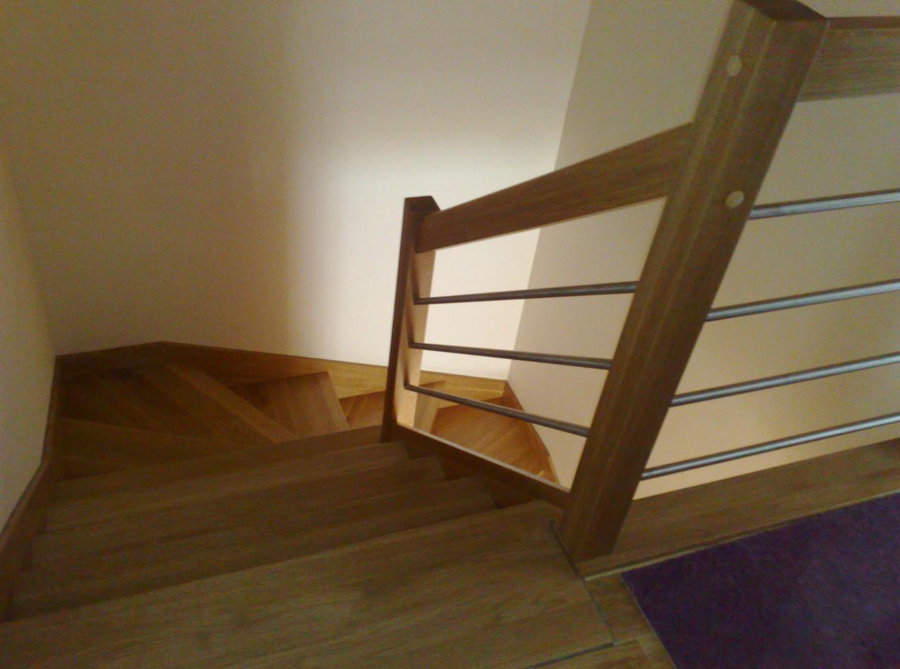 Drewniane schody z metalową balustradą widziane z góry, z widocznym fioletowym dywanikiem na dole kadru.