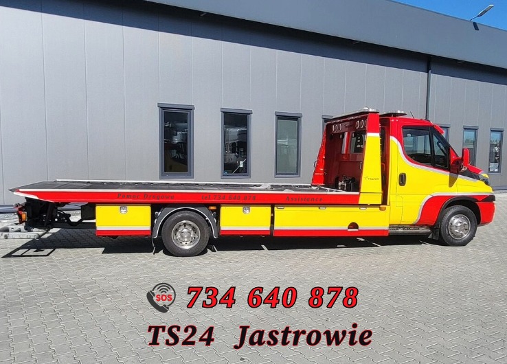 Żółto-czerwona laweta na tle szarej hali z oknami. Widoczny numer telefonu i nazwa firmy 'TS24 Jastrowie'.