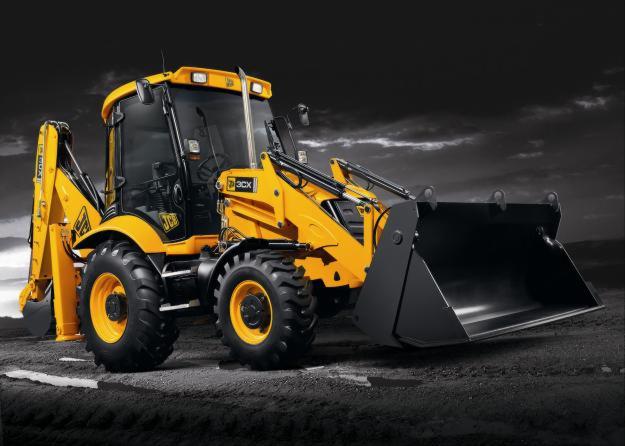 Żółta koparko-ładowarka JCB 3CX na ciemnym, lekko nierównym podłożu z czarno-białym, pochmurnym tłem.