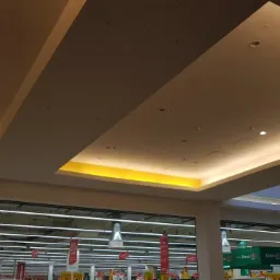 Sufit podwieszany z oświetleniem LED w supermarkecie, widok od dołu, widoczne elementy konstrukcyjne i oświetleniowe.