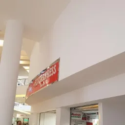 Wnętrze galerii handlowej z białymi ścianami i kolumną, widoczny szyld 'FOTO EXPRESS' i fragment drugiego poziomu z balustradą.