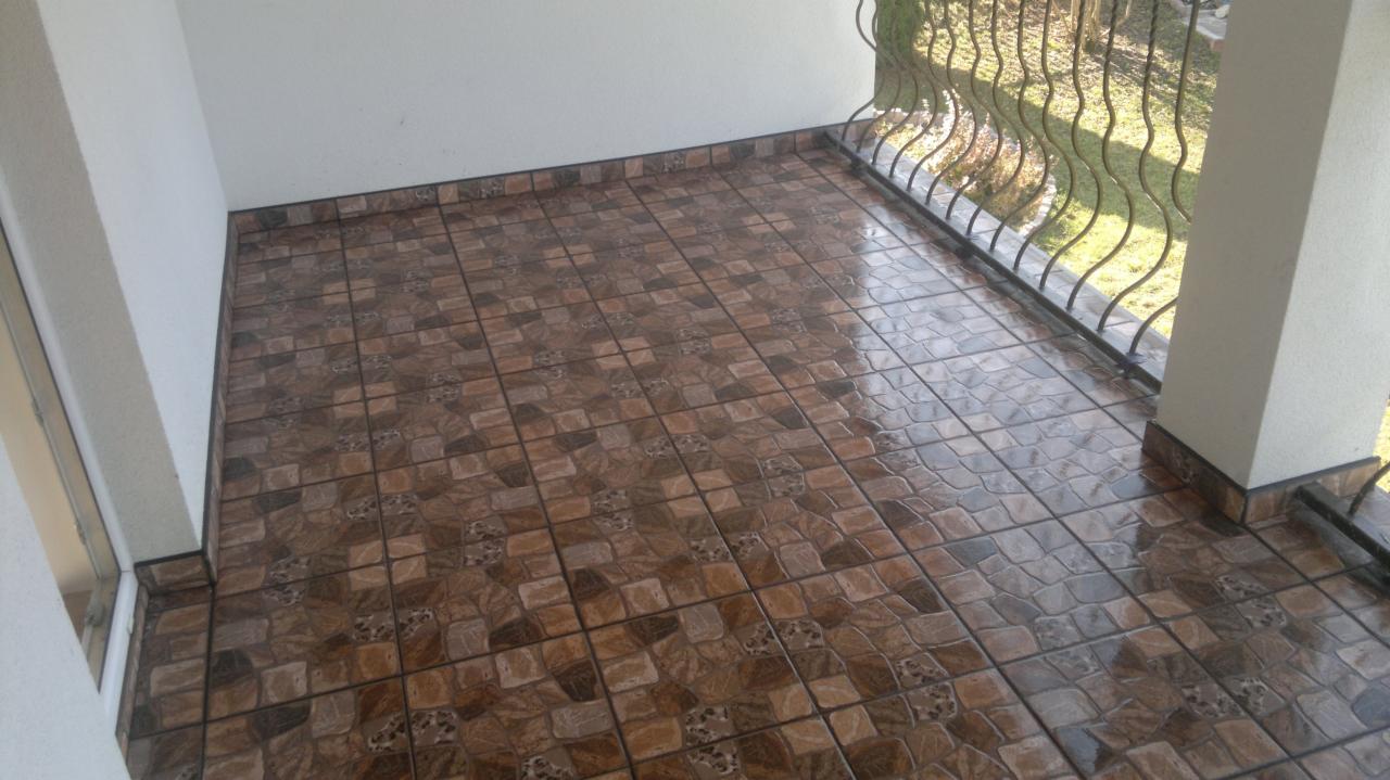 Ułożona podłoga z brązowych płytek na balkonie, widoczna barierka i filar.