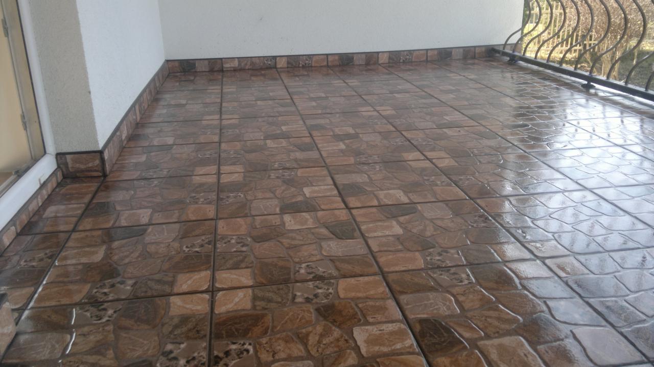 Wykończony balkon z brązowymi płytkami imitującymi kamień, z widoczną balustradą i fragmentem elewacji budynku.