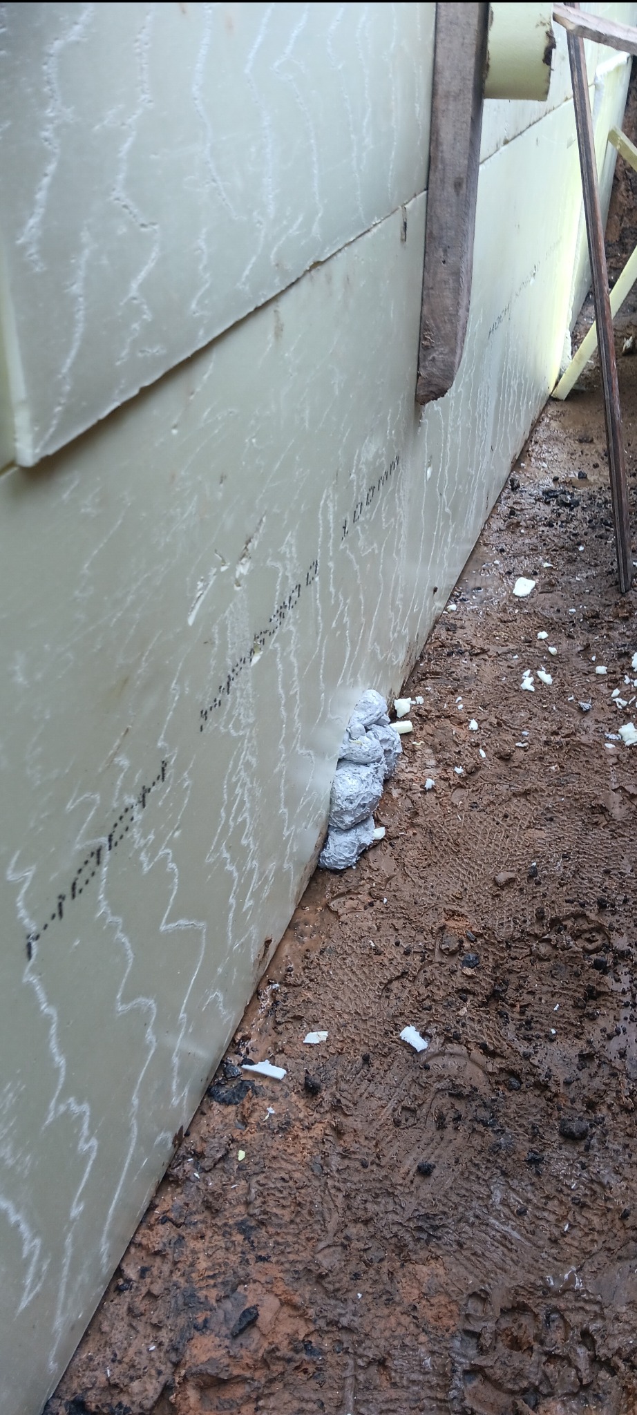 Izolacja pionowa fundamentu z widocznymi oznaczeniami i zabezpieczeniem pianką montażową, grunt w stanie surowym.