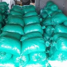 Stosy worków z zawartością w intensywnym turkusowym kolorze, ułożone równo w trzech kolumnach wewnątrz przyczepy, z widocznymi sznurkami wiążącymi.