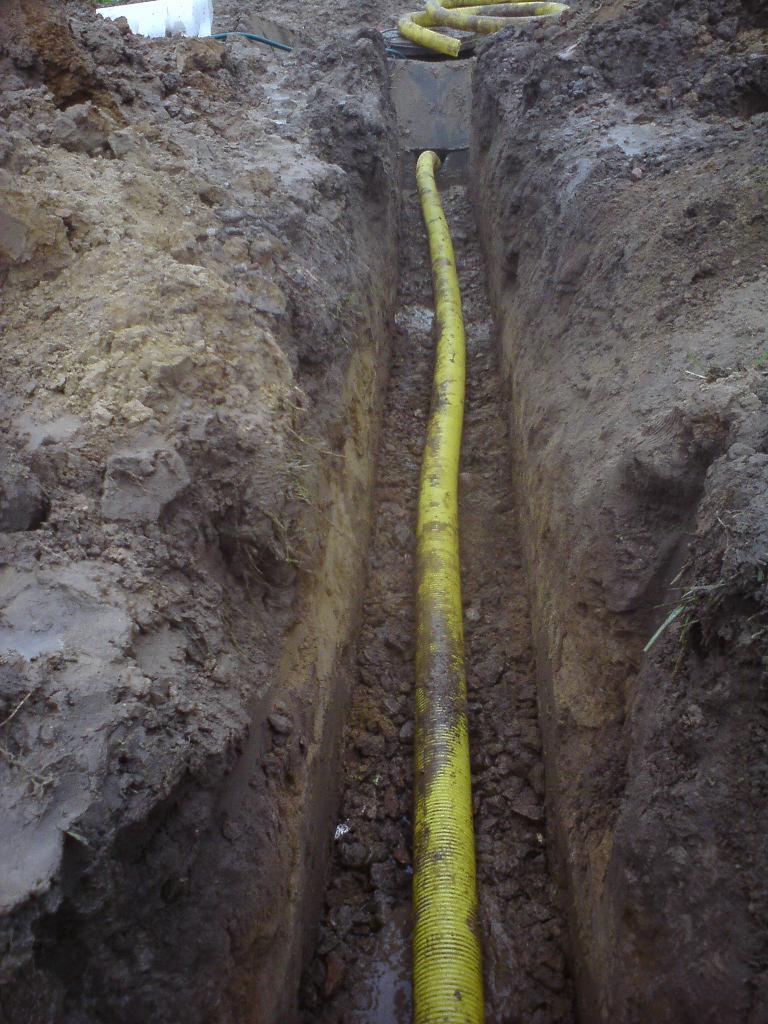 Żółta rura drenarska ułożona w wykopie w ziemi, widoczny fragment systemu drenarskiego.