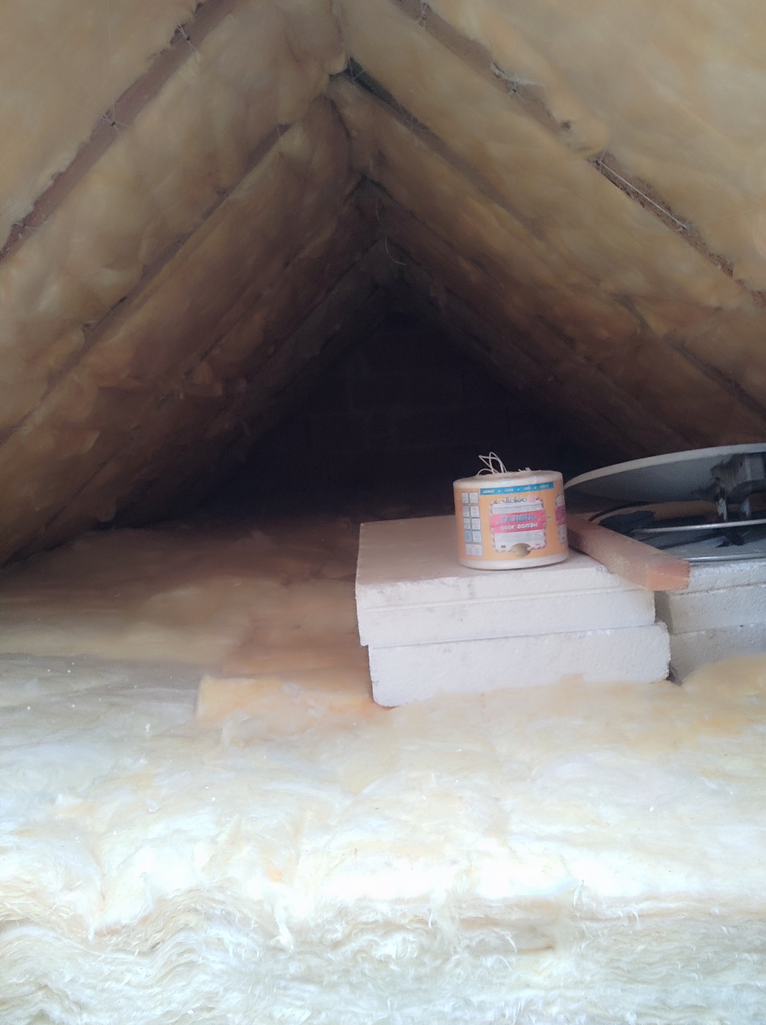 Ocieplone poddasze wełną mineralną, widoczne krokwie i elementy wentylacji. Na pierwszym planie styropian i puszka z klejem.