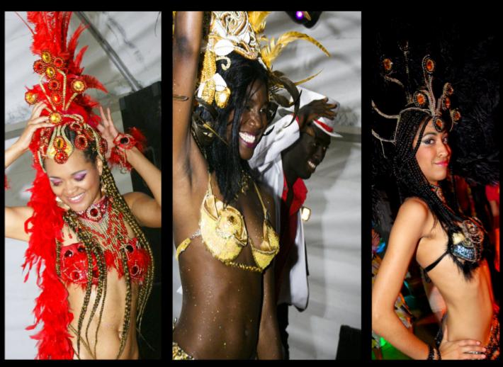 Trzy tancerki w barwnych, karnawałowych strojach: czerwonym z piórami, złotym brokatowym i czarnym z piórami, prezentują się na tle sceny podczas pokazu.