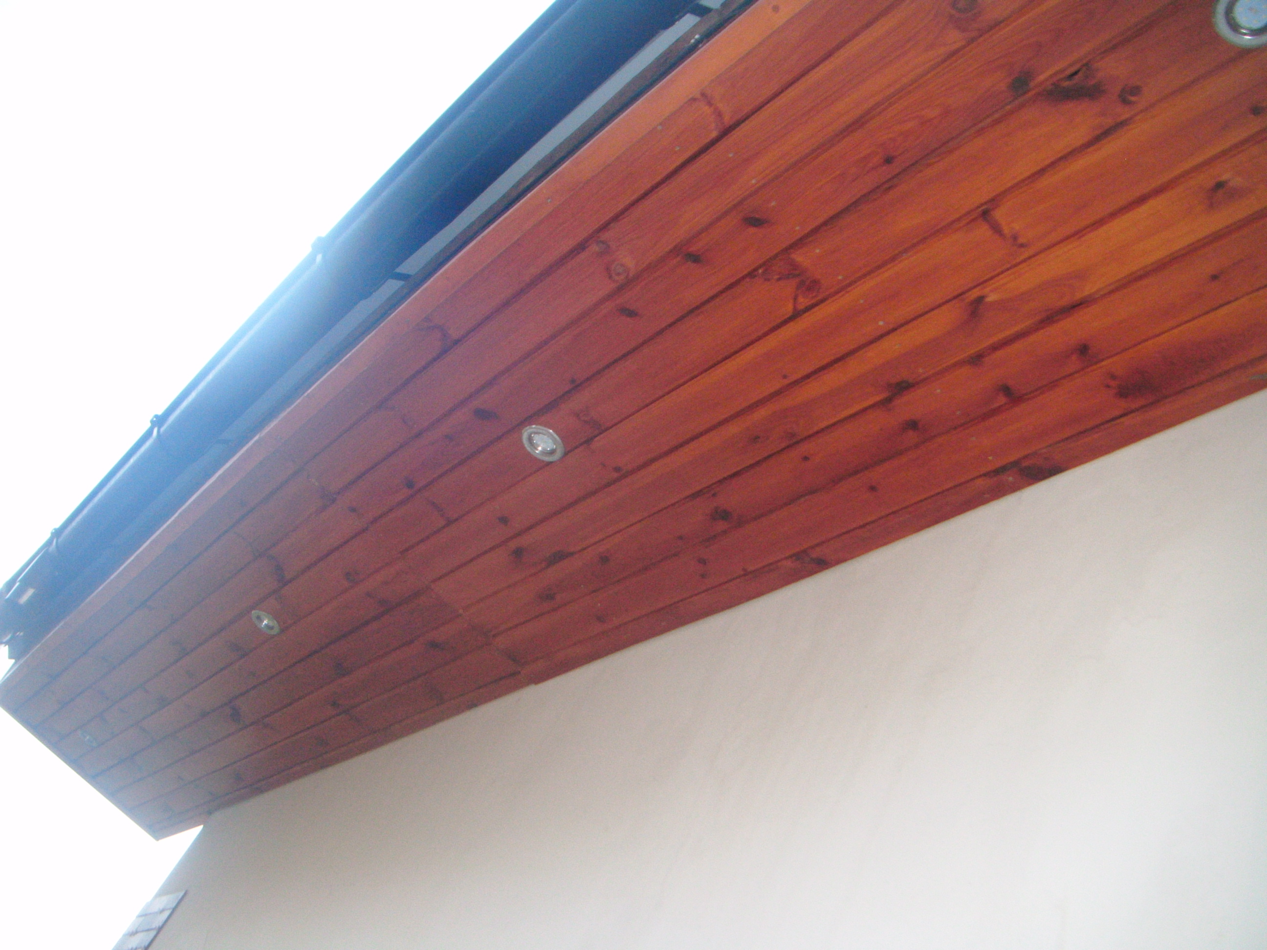 Drewniana podbitka dachowa z wbudowanymi punktowymi lampami, widok z dołu na fragment elewacji.