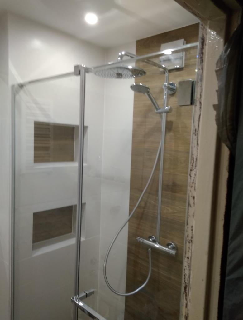 Kabina prysznicowa z deszczownicą i baterią termostatyczną, wykończona płytkami imitującymi drewno, widoczne niedokończone obramowanie kabiny.