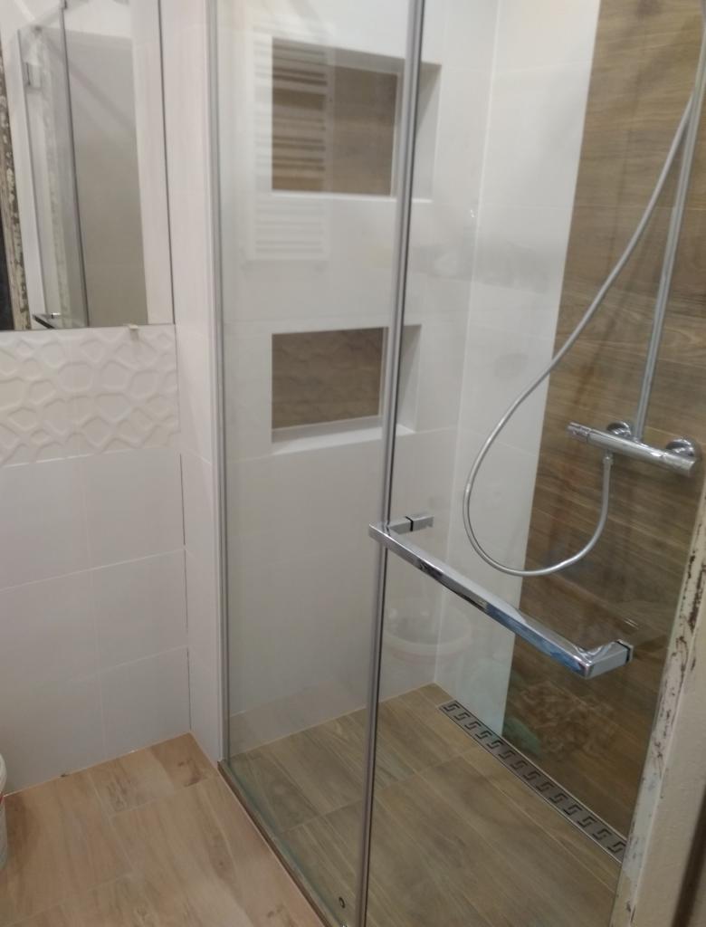 Nowoczesna kabina prysznicowa z chromowanymi detalami, drewnopodobne płytki podłogowe i ścienne w odcieniach beżu i brązu, wbudowane półki w ścianie, odpływ liniowy.