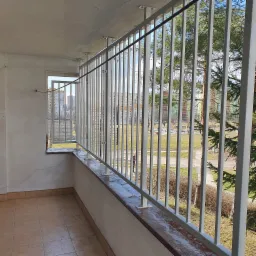 Szara metalowa balustrada balkonowa z pionowymi prętami, widok na osiedle mieszkaniowe i plac zabaw w tle.