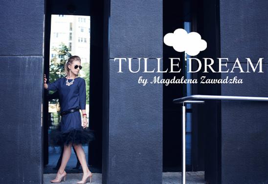 Kobieta w granatowej sukience z tiulowym dołem, pozująca w ciemnym przejściu. Widoczny napis 'Tulle Dream by Magdalena Zawadzka' i grafika chmurki.