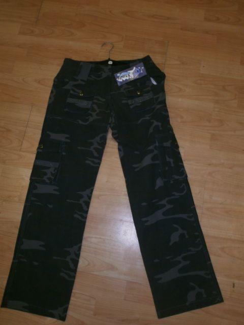 Spodnie damskie moro z metką, leżące na podłodze z paneli, widoczne kieszenie cargo i metalowe guziki.