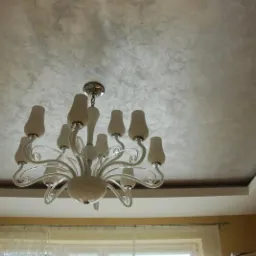 Dekoracyjny sufit w odcieniach szarości z efektem marmuru, oświetlony przez elegancki, biały żyrandol. Widoczna listwa przysufitowa.