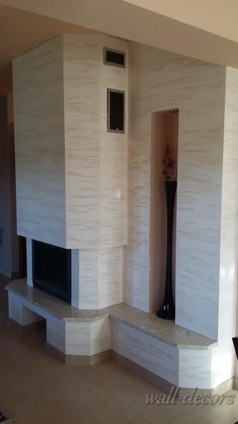 Obudowa kominka z płyt w odcieniach beżu i bieli, z wnęką na dekorację. Widoczne detale wykończenia i imitacja marmuru na powierzchni płyt.