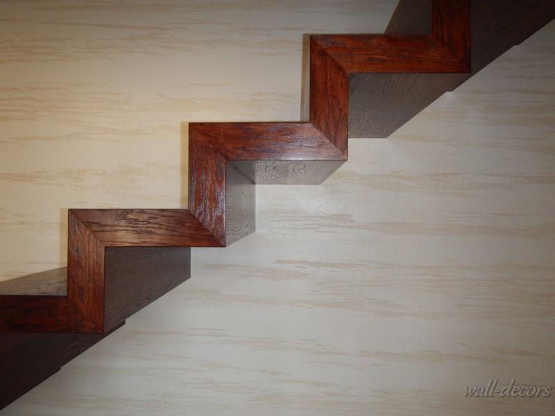 Schody z ciemnego drewna, zamontowane na ścianie z delikatnym, poziomym wzorem, widoczne z bliska pod kątem, z wyraźnym cieniem pierwszego stopnia.